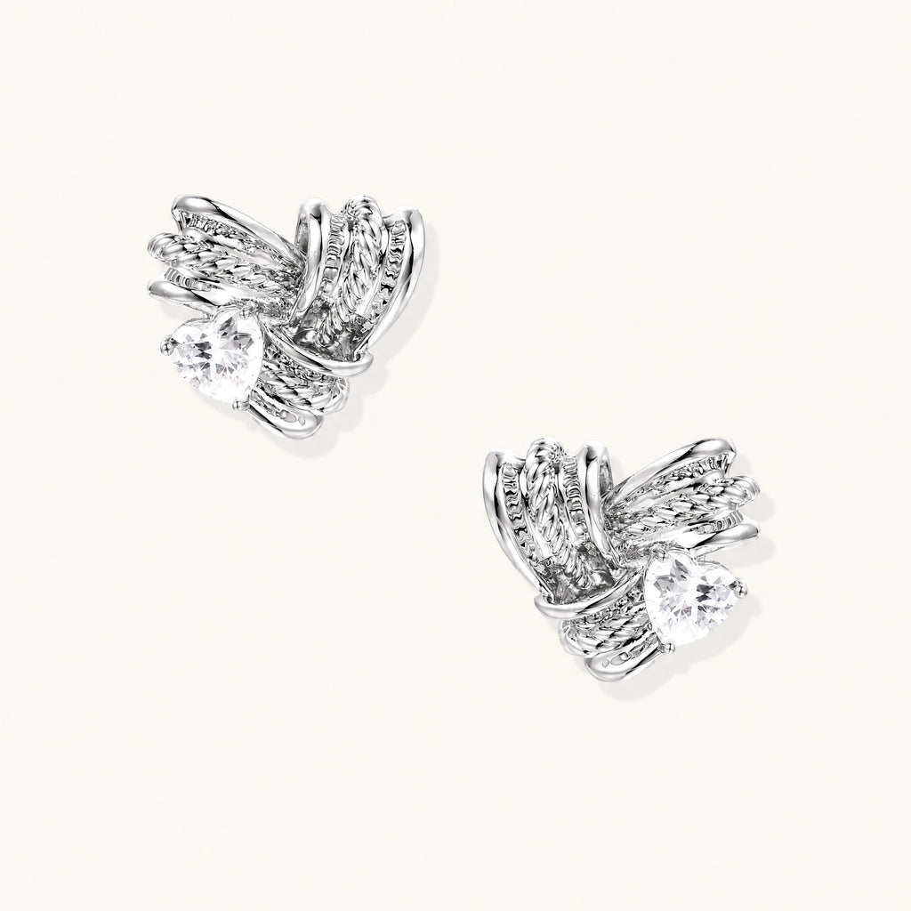 Pair of sculptural white gold-plated stud earrings with twisted ribbon design and sparkling zirconia stones on cream background