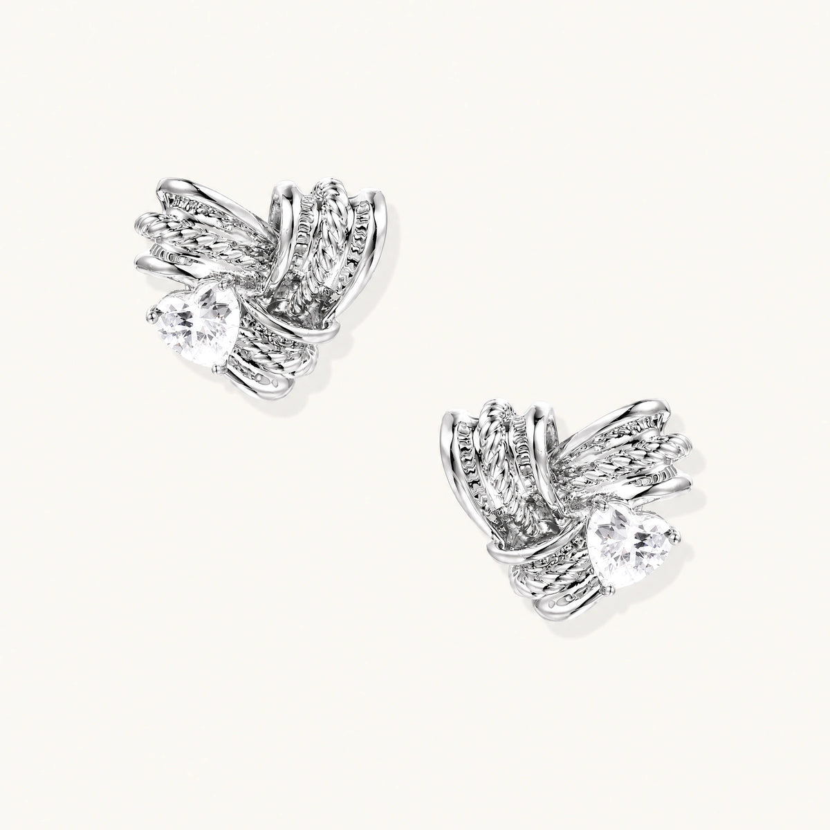 Pair of sculptural white gold-plated stud earrings with twisted ribbon design and sparkling zirconia stones on cream background