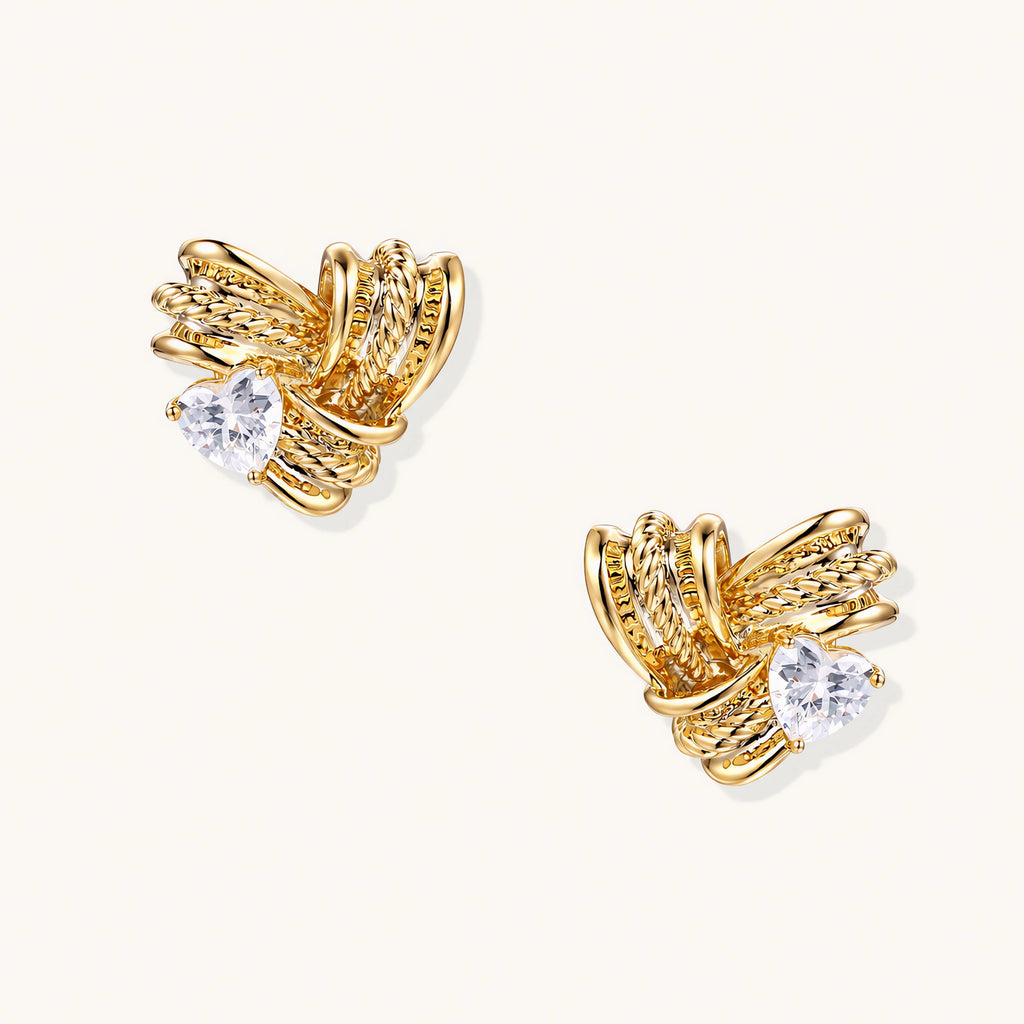 Pair of sculptural gold-plated wing stud earrings with zirconia stones on cream background, showing dimensional feather design
