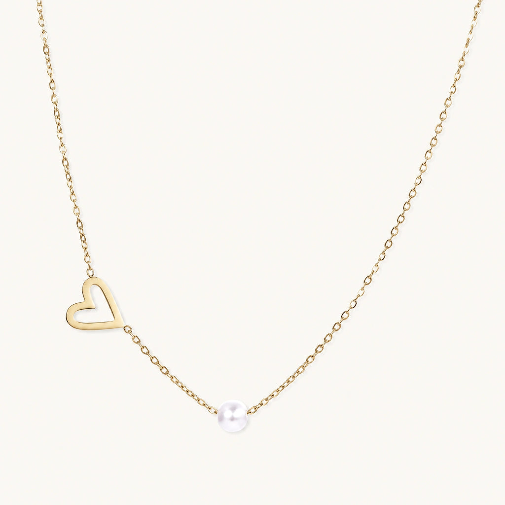 Dainty 14K gold plated stainless steel necklace with an open heart charm and a single round white bead on a cream background.