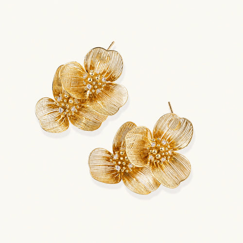 Pair of gold-plated double flower earrings with textured petals and crystal centers on cream background.